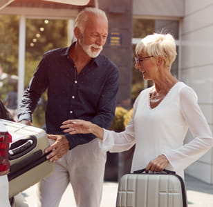 A couple loading a suitcase in to the boot of their car